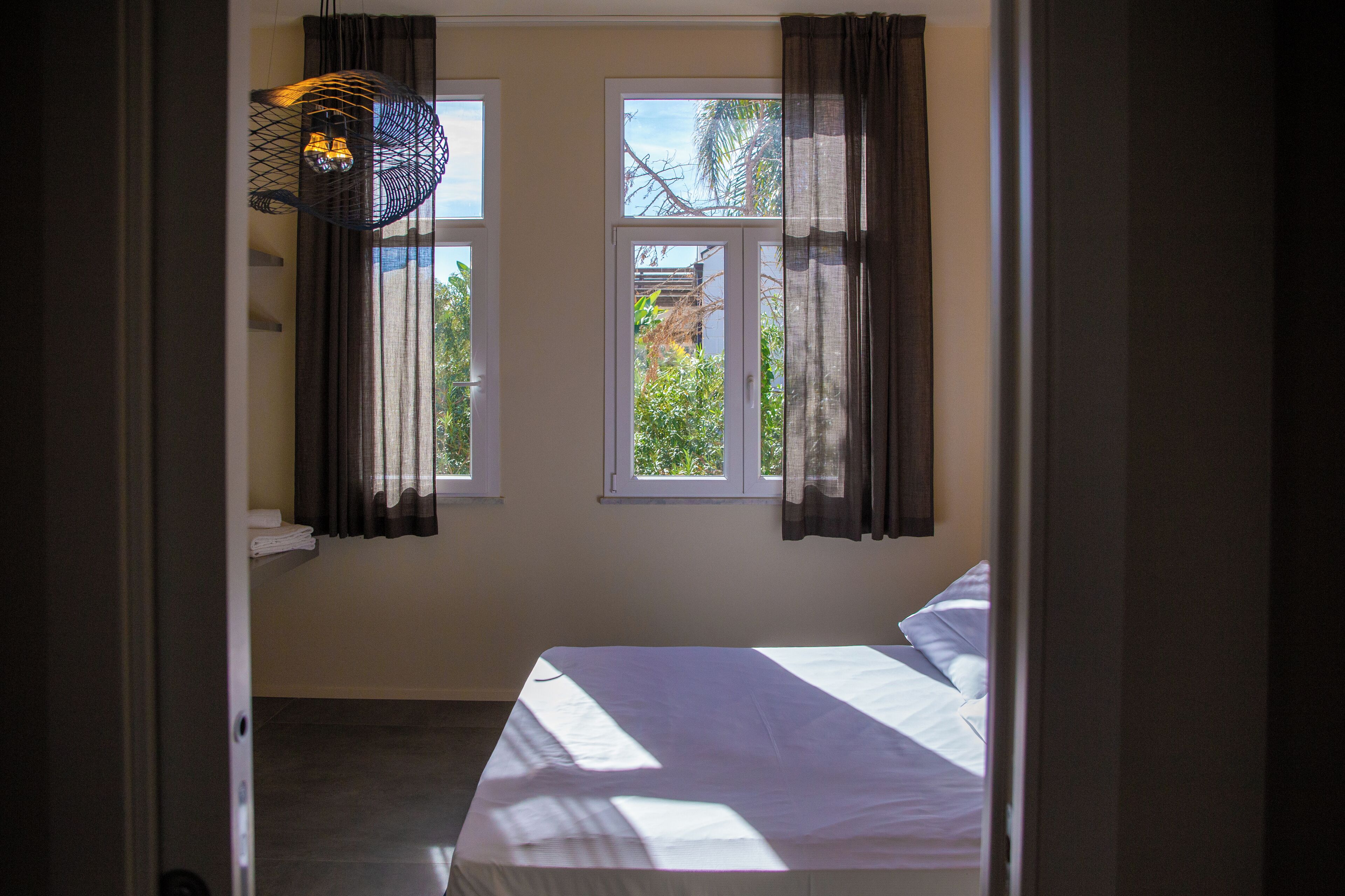 Ein Schlafzimmer mit einem Bett, zwei Fenstern und einer Pendelleuchte.
