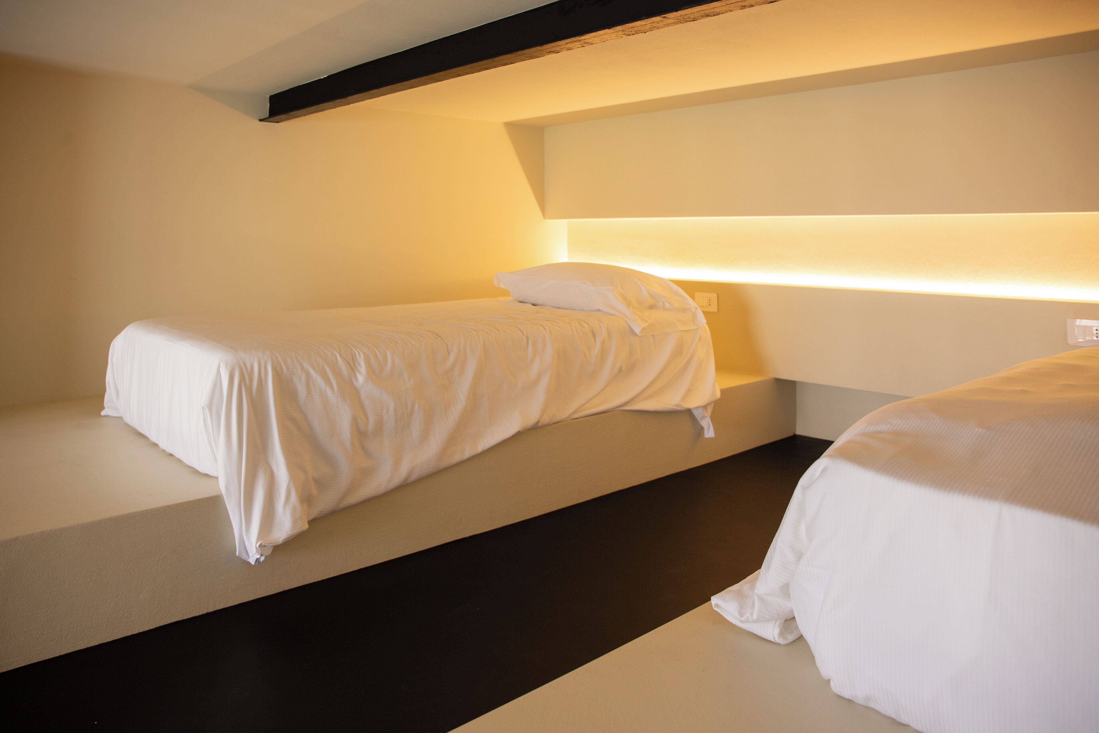 Hotellihuone, jossa on kaksi erillistä sänkyä, tumma lattia ja pelkistetty, siisti sisustus.