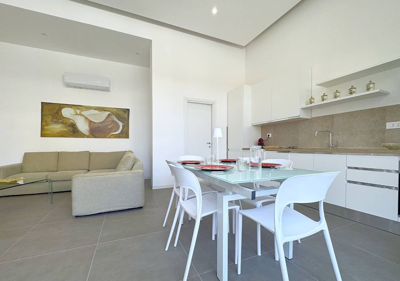 Una sala de estar moderna con un sofá, una mesa de comedor de vidrio con sillas, y una zona de cocina con armarios y una encimera.