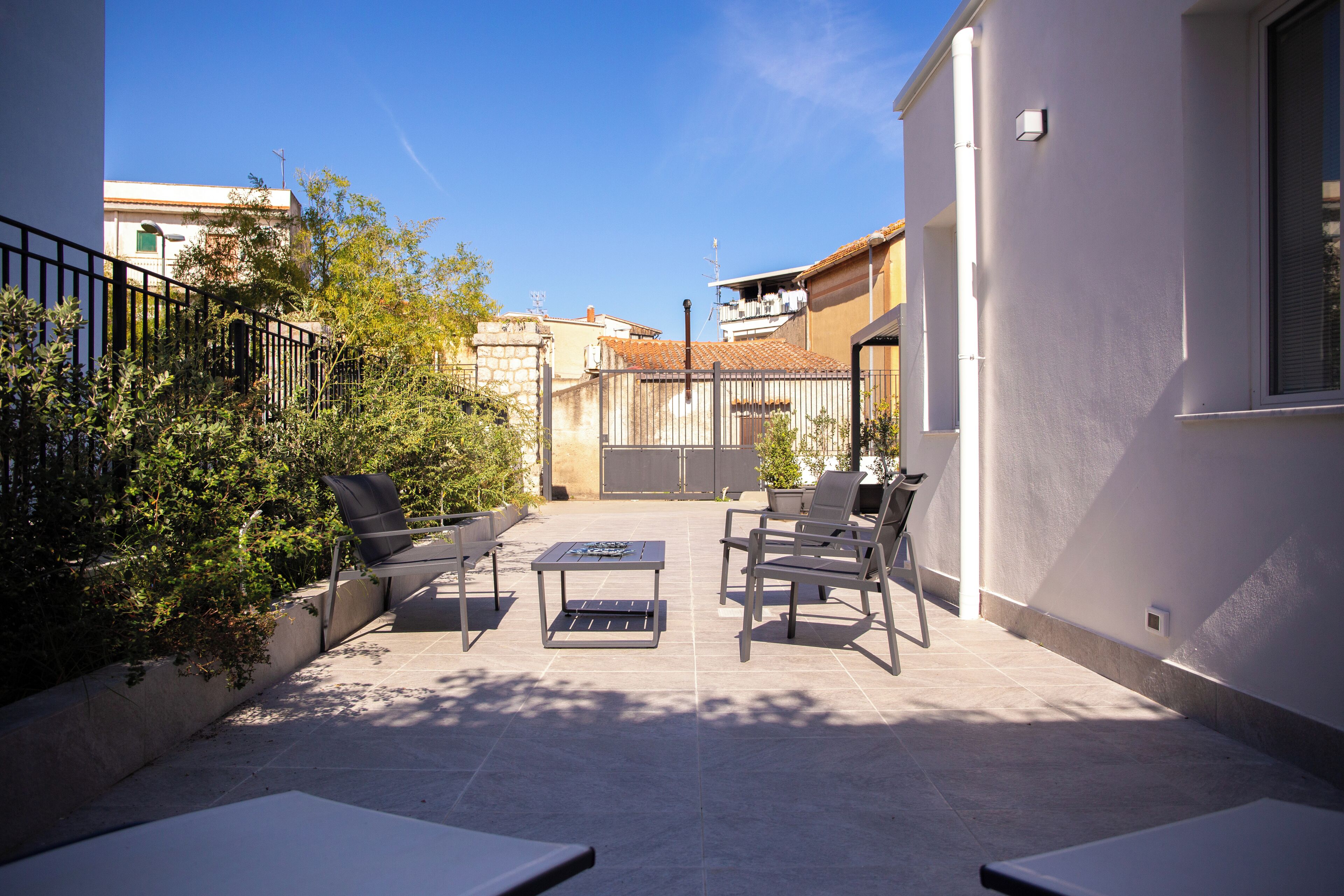 An outdoor patio with a table and chairs, surrounded by a low wall and vegetation.
