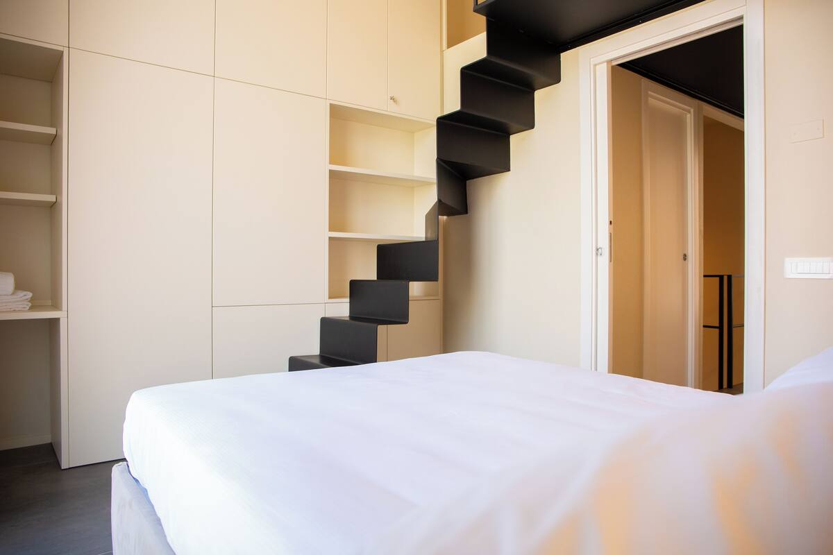 Une chambre à coucher avec un lit, une armoire blanche et un escalier noir.