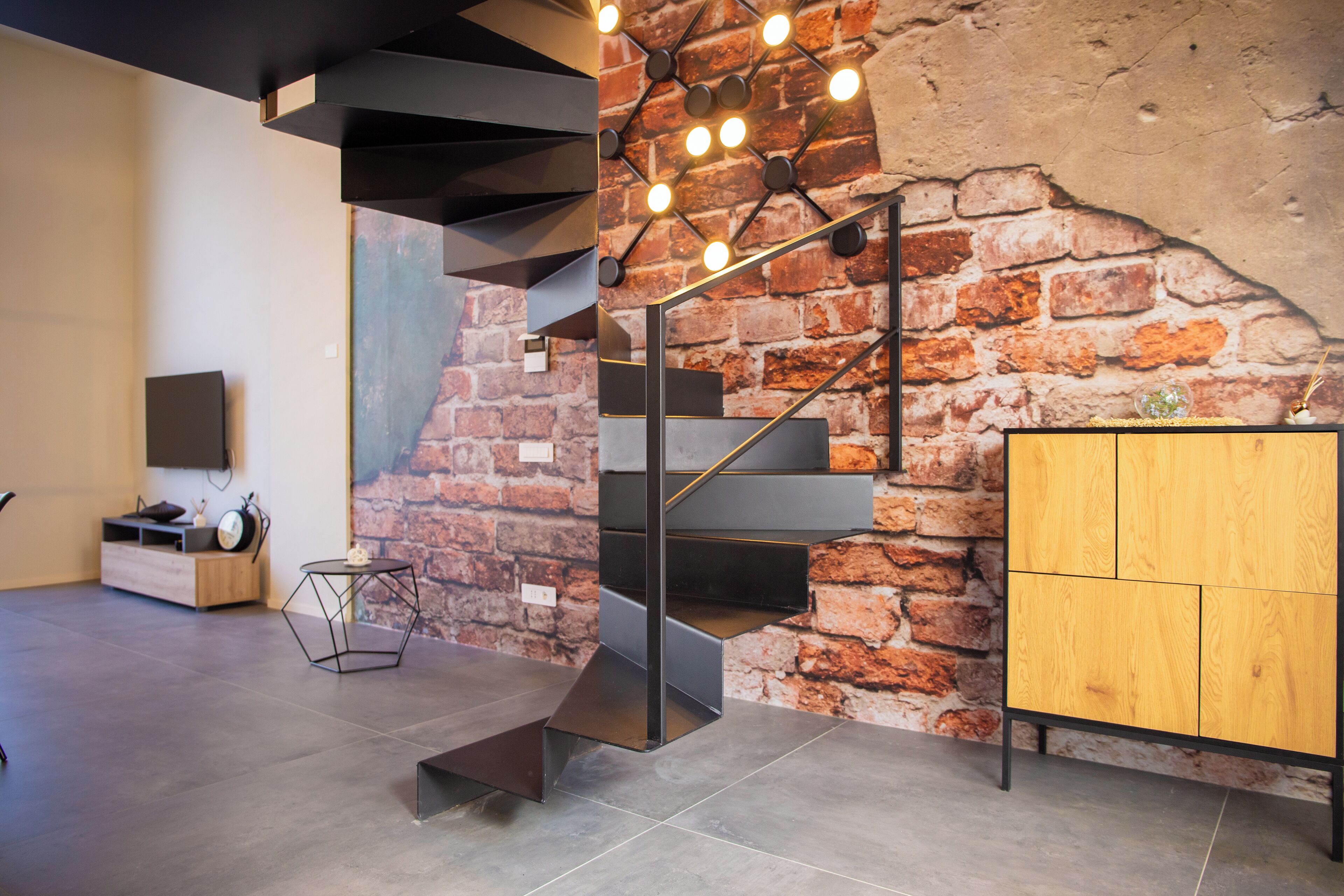 A modern interior with a brick wall, a staircase, a wooden cabinet, and a hexagonal table.