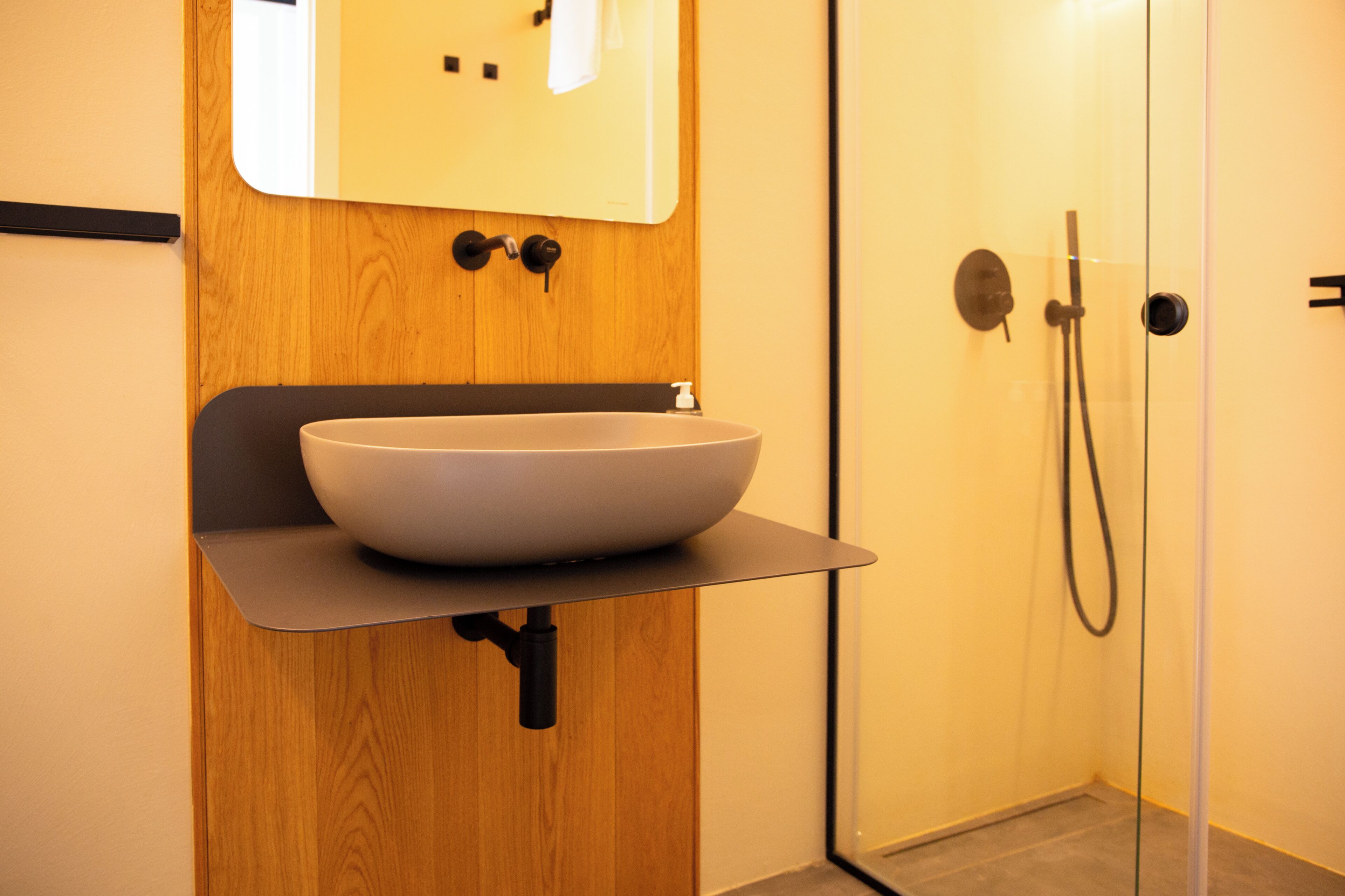 A modern bathroom with a wooden vanity, a large vessel sink, and a glass-enclosed shower area.