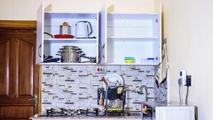 Una cocina con armarios blancos, salpicadero de azulejos y microondas. Hay una estufa, un fregadero y diversos utensilios de cocina.