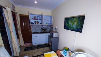 Una cocina compacta con estufa a gas, microondas y un refrigerador pequeño. Hay una zona de comedor con mesa y sillas, y un televisor de pared.