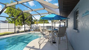 A covered outdoor pool area with a table and chairs, a blue umbrella, and a poolside sign. - FOX's Hidden Oasis 2 BR Pool Home 3 miles to AMI beaches (Bradenton)