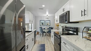 A modern kitchen with white cabinets, a stainless steel refrigerator, a microwave, and a stove. There is a dining table with chairs and a rug on the floor. - FOX's Hidden Oasis 2 BR Pool Home 3 miles to AMI beaches (Bradenton)