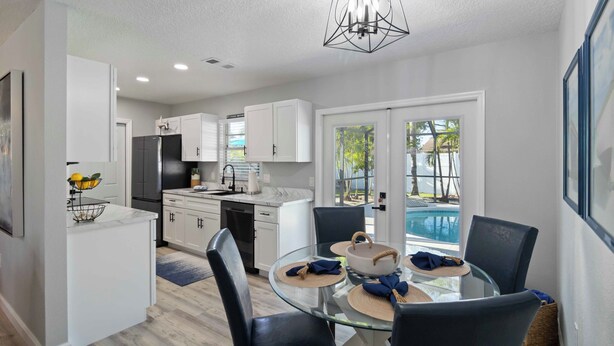 A modern kitchen with white cabinets, a stainless steel refrigerator, and a dining area with a glass table and black chairs. - FOX's Hidden Oasis 2 BR Pool Home 3 miles to AMI beaches (Bradenton)