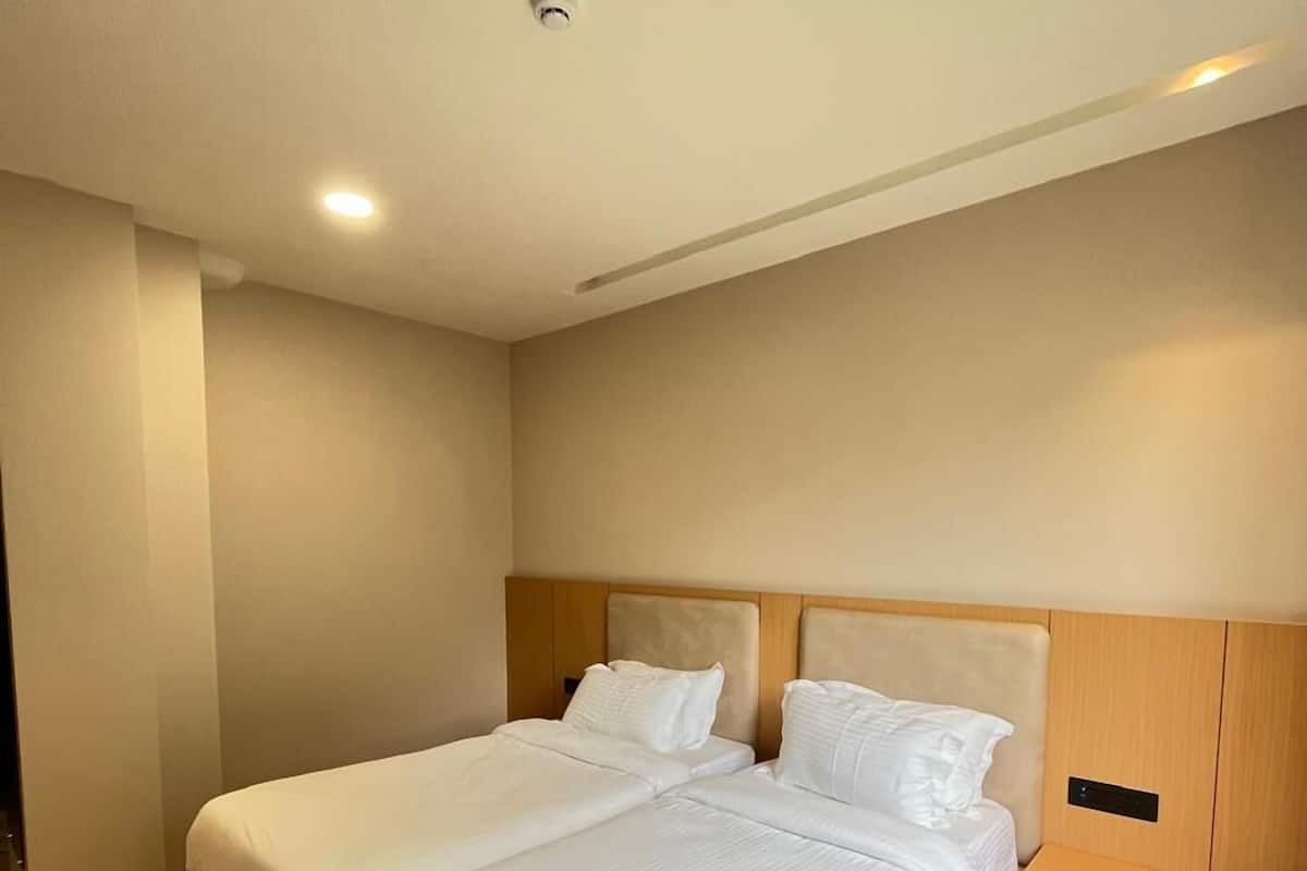 A modern hotel room with a large bed, a nightstand, and a wall-mounted control panel.