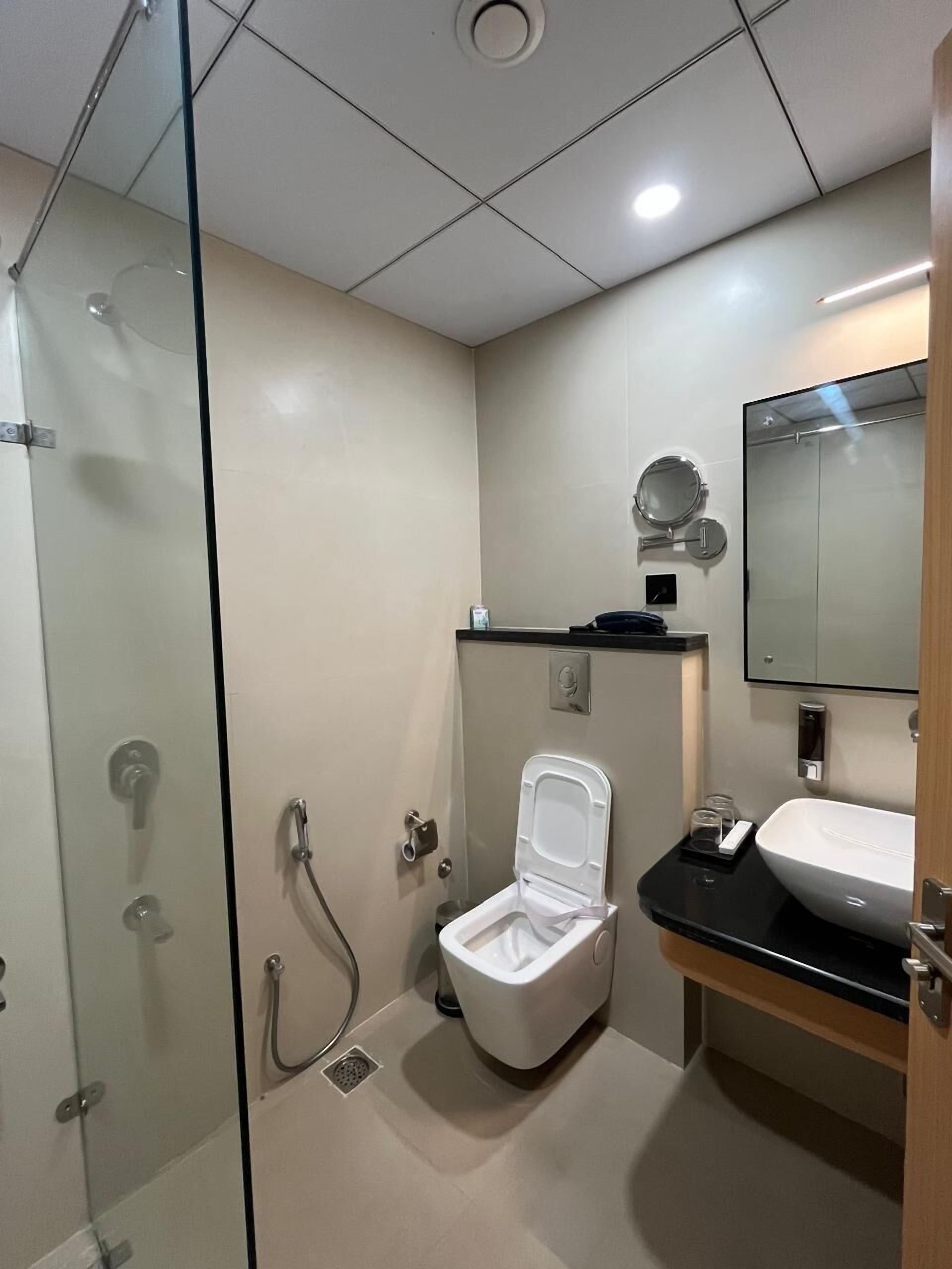 Een moderne badkamer met een douchecabine van glas, een wit toilet en een wastafel met een spiegel erboven.