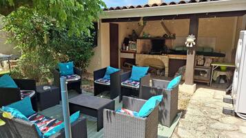 Un'area patio esterna con mobili in vimini e cuscini blu, un camino in pietra e un tetto in tegole.