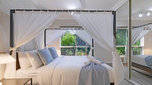 Ein Schlafzimmer mit Himmelsbett, Nachttisch, Lampe und einem großen Spiegel.