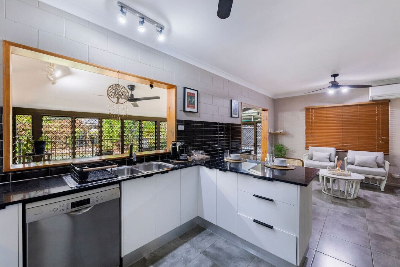 Una cucina moderna con mobili bianchi, un piano di lavoro nero e una finestra vista verde.