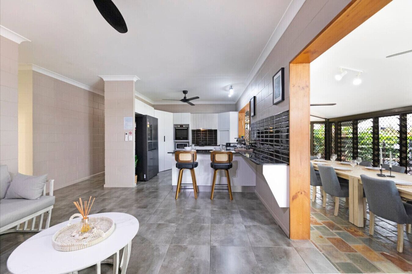 A modern kitchen with a dining area, featuring a central island, bar stools, and a long dining table.