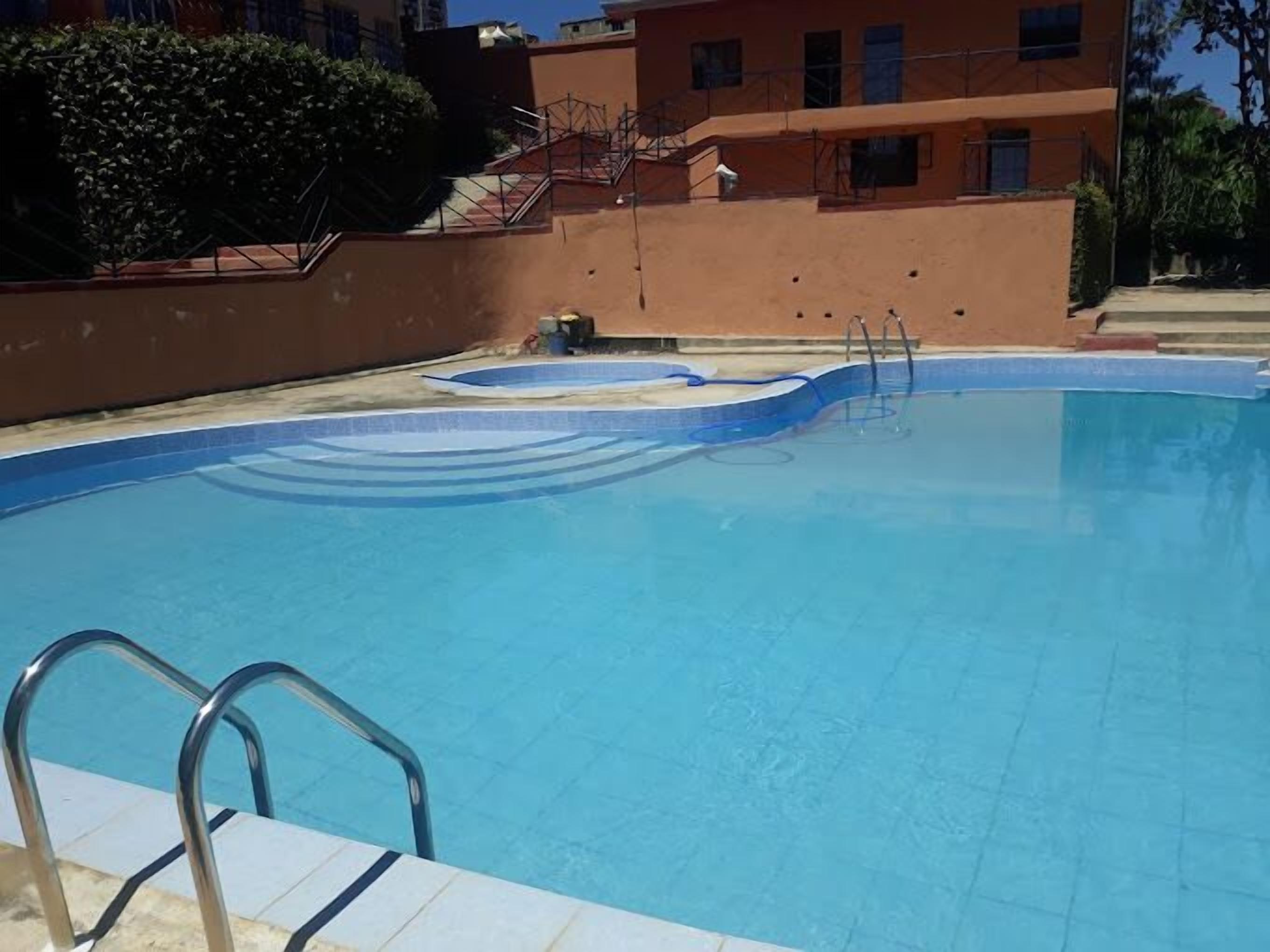 Une piscine à l’eau d’un bleu limpide, entourée d’un petit muret et dotée d’une échelle en métal.
