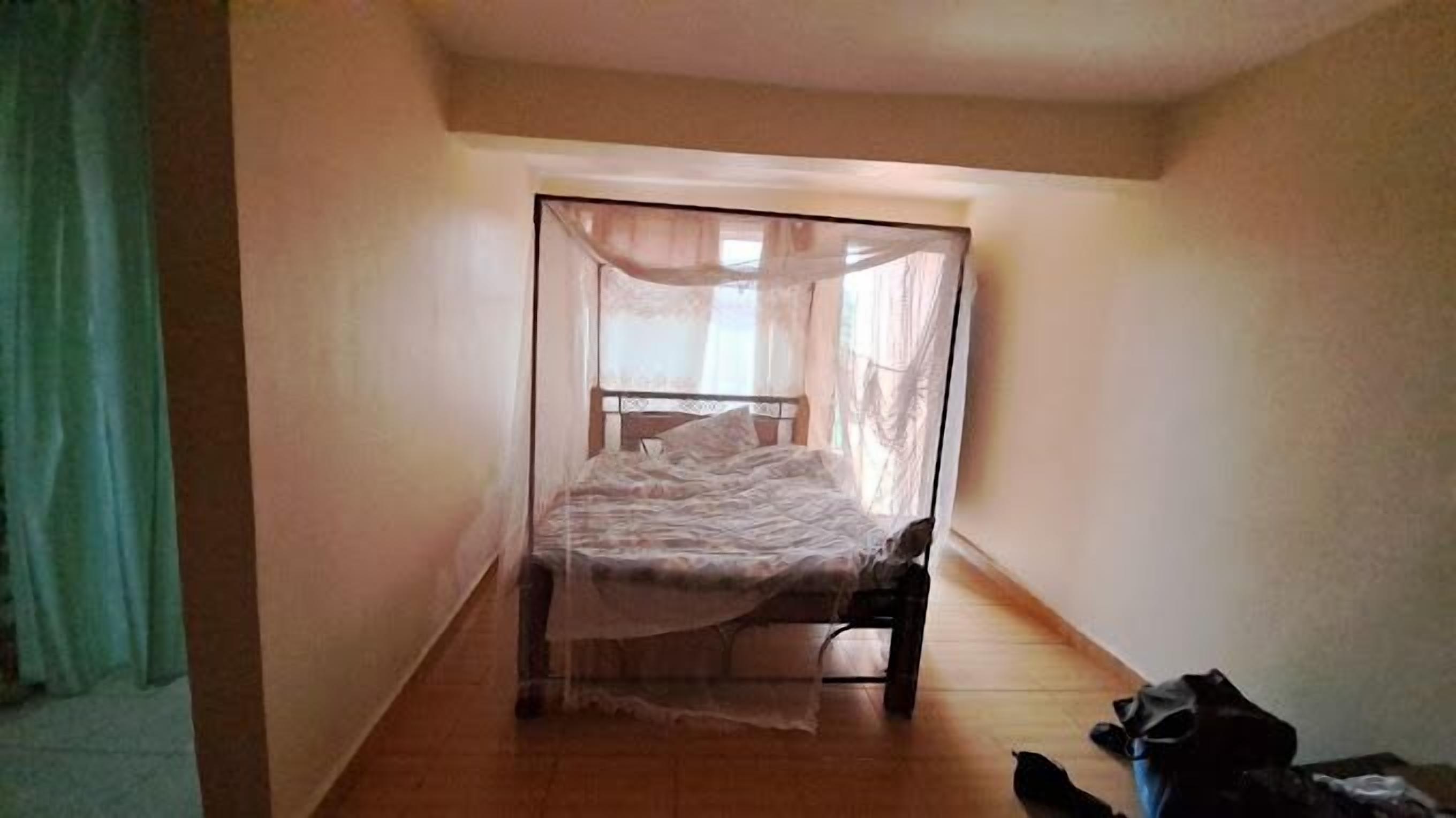 A narrow room with a bed covered by a sheer canopy.