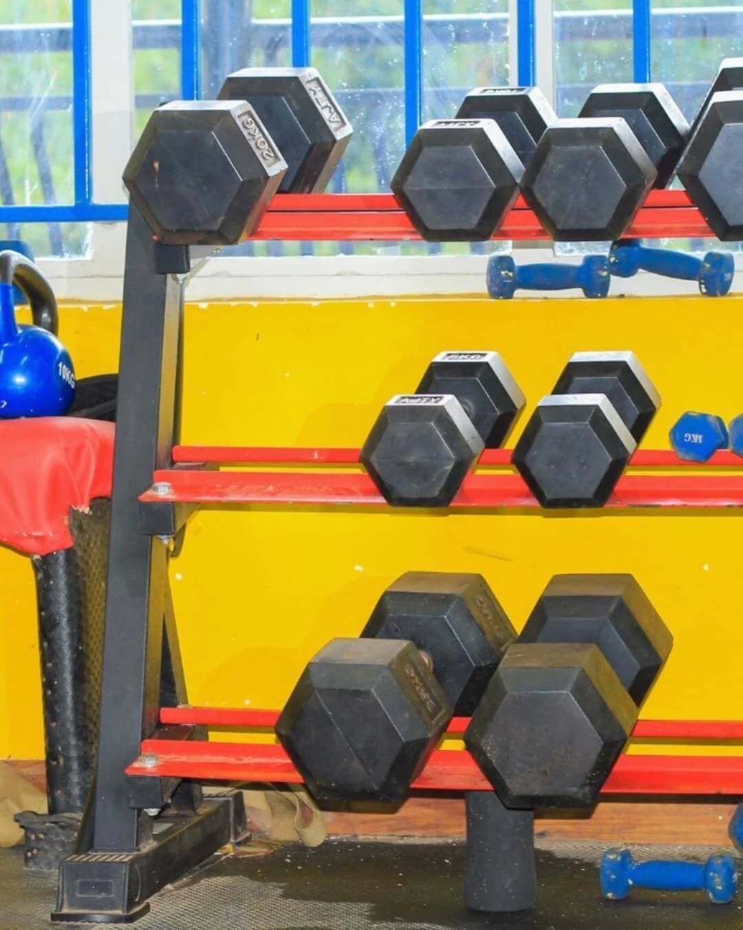 A rack of hexagonal dumbbells in a gym with a yellow and red color scheme.