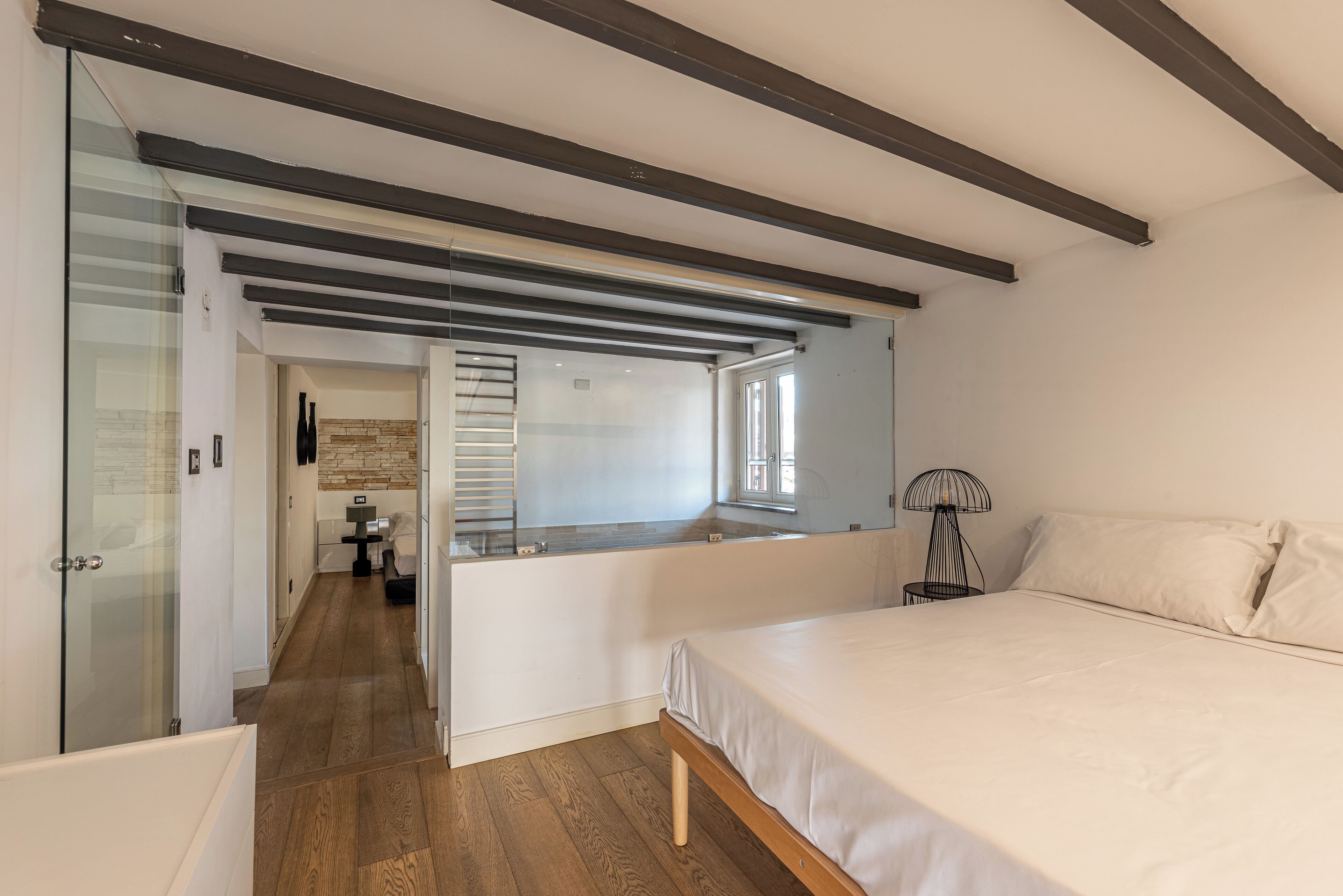 A modern bedroom with a large bed, a glass shower enclosure, and a wooden floor.