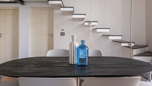 A modern conference room with a dark marble table, white chairs, a blue vase, and a white vase. A staircase with built-in shelves is visible in the background. - Appartamento Sammartino by Wonderful Italy (Palermo)