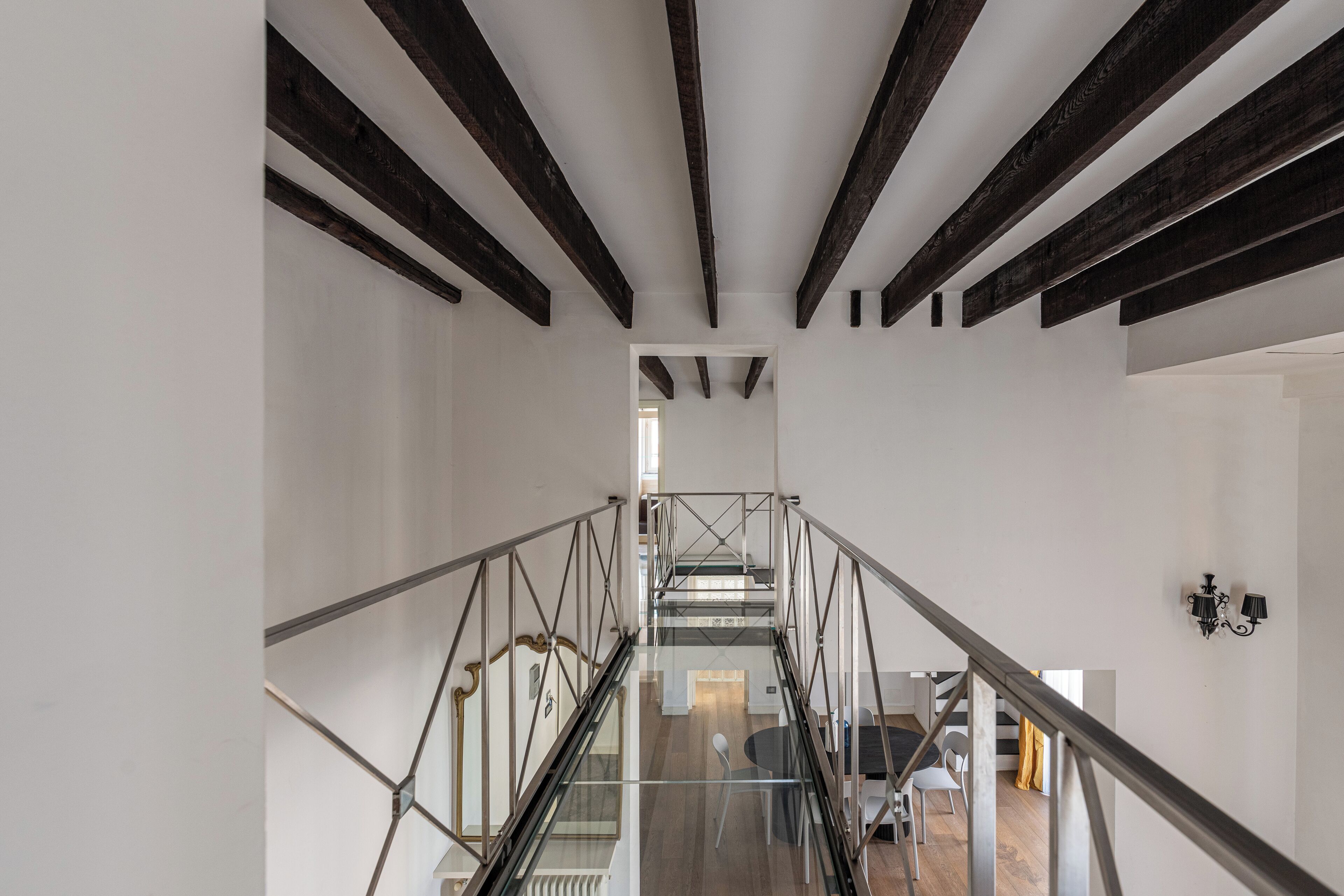 Un interior moderno con una escalera de cristal, paredes blancas y vigas de madera a la vista.