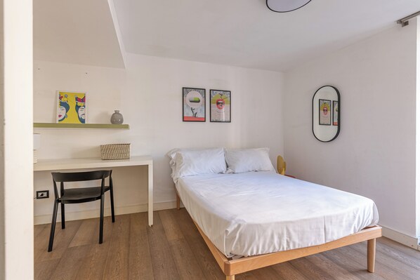 A bedroom with a bed, a desk, a chair, and two framed artworks on the wall.