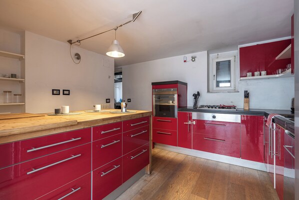 A modern kitchen with red cabinetry, a wooden countertop, and a built-in oven.