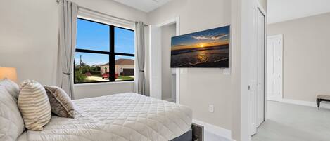 A bedroom with a large bed, a TV mounted on the wall, and a window with curtains.