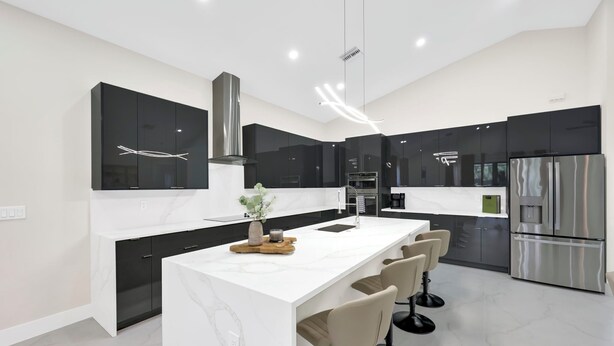Una cocina moderna con una isla central, armarios negros, electrodomésticos de acero inoxidable y encimera de mármol.