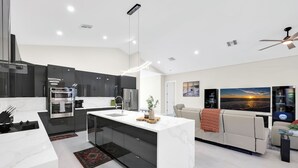 Una cocina moderna con una isla central, electrodomésticos integrados y un comedor con sofá y obras de arte.