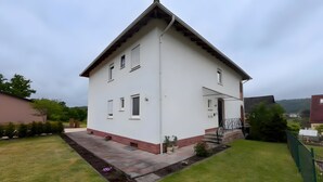 Una casa blanca de dos pisos con techo inclinado, un pequeño porche y un césped bien cuidado.