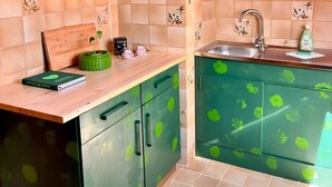 Una cocina con armarios verdes, encimera de madera y salpicadero de azulejos con motivos florales.