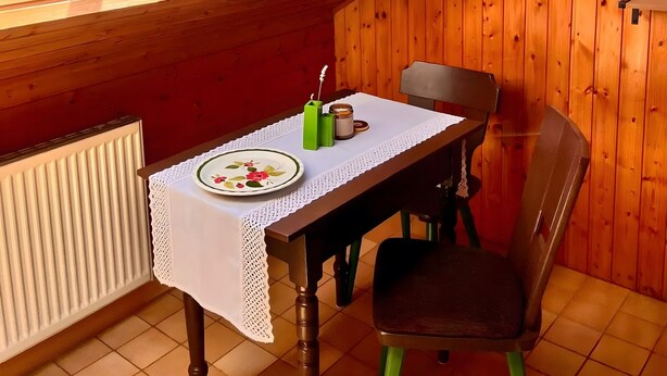 Habitación con paneles de madera, una mesa dispuesta para dos personas, una silla, un radiador y vistas a través de un tragaluz.
