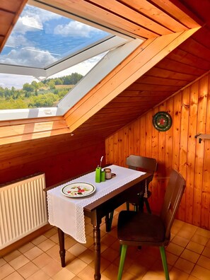 A wooden-paneled room with a table set for two, a chair, a radiator, and a view through a skylight. - Apartment 'Daniela Fellen - Magda' with Mountain View, Shared Terrace and Wi-Fi (Fellen)