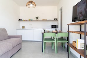 Une cuisine moderne avec des meubles blancs, un four à micro-ondes et un coin repas agrémenté de deux chaises vertes.