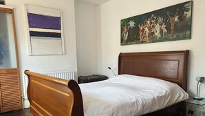 A bedroom with a wooden bed, a radiator, a painting, and a desk with a lamp. - Traditional Victorian house (Hastings)
