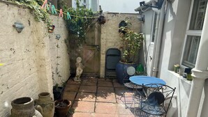A courtyard with a blue metal table and chairs, a stone statue, potted plants, and a wooden gate. - Traditional Victorian house (Hastings)
