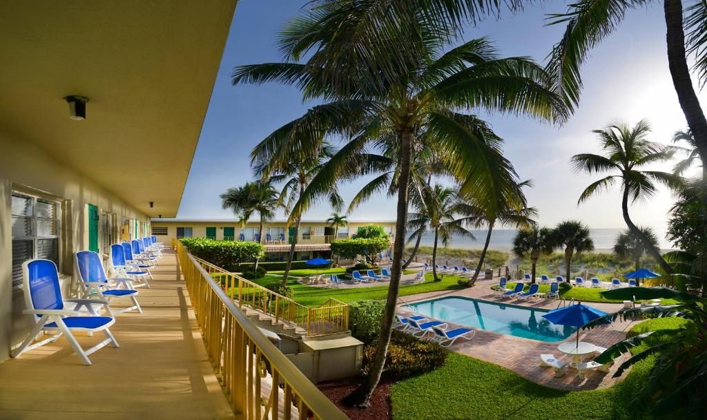 Un balcón de hotel con piscina, sillas de descanso y palmeras.