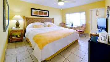 A hotel room with a bed, a desk with a chair, a television, and a ceiling fan.
