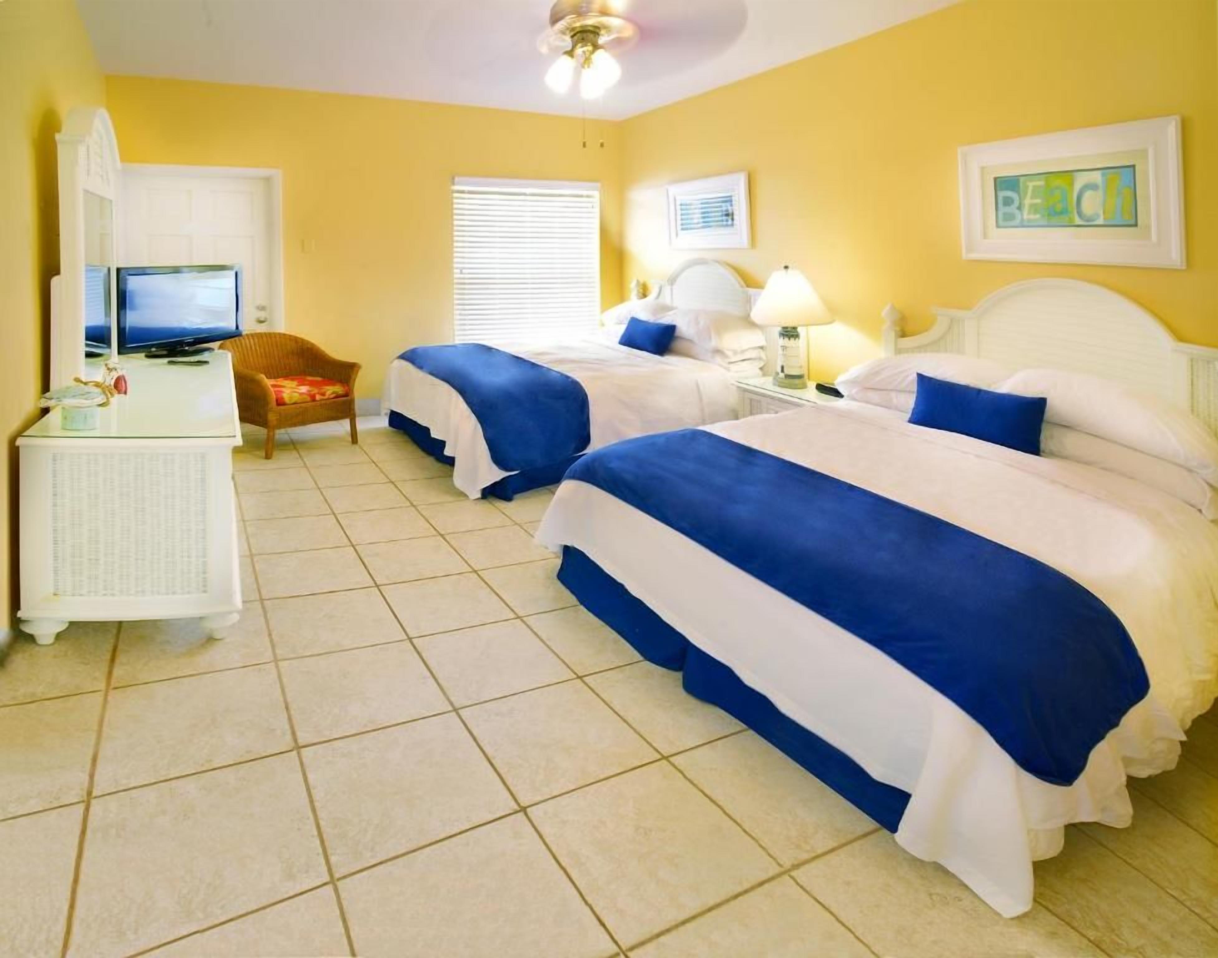 A hotel room with two beds, a television, a desk, and a chair.