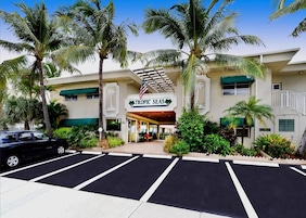 Un hotel con un letrero que dice 'TROPIC SEAS' y un estacionamiento al frente.