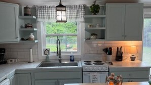 A kitchen with white cabinets, a wooden countertop, a stove, and a window with a view of greenery. - Storybook Chatham (Newport)