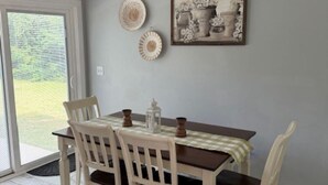 A dining area with a table set for four, surrounded by white chairs. There is a chandelier above the table, and a framed picture hangs on the wall. - Storybook Chatham (Newport)