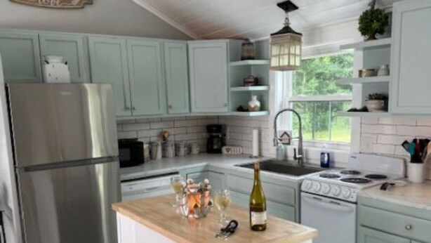 A kitchen with light green cabinets, a wooden countertop, a stainless steel refrigerator, a stove, and a wine bottle. - Storybook Chatham (Newport)