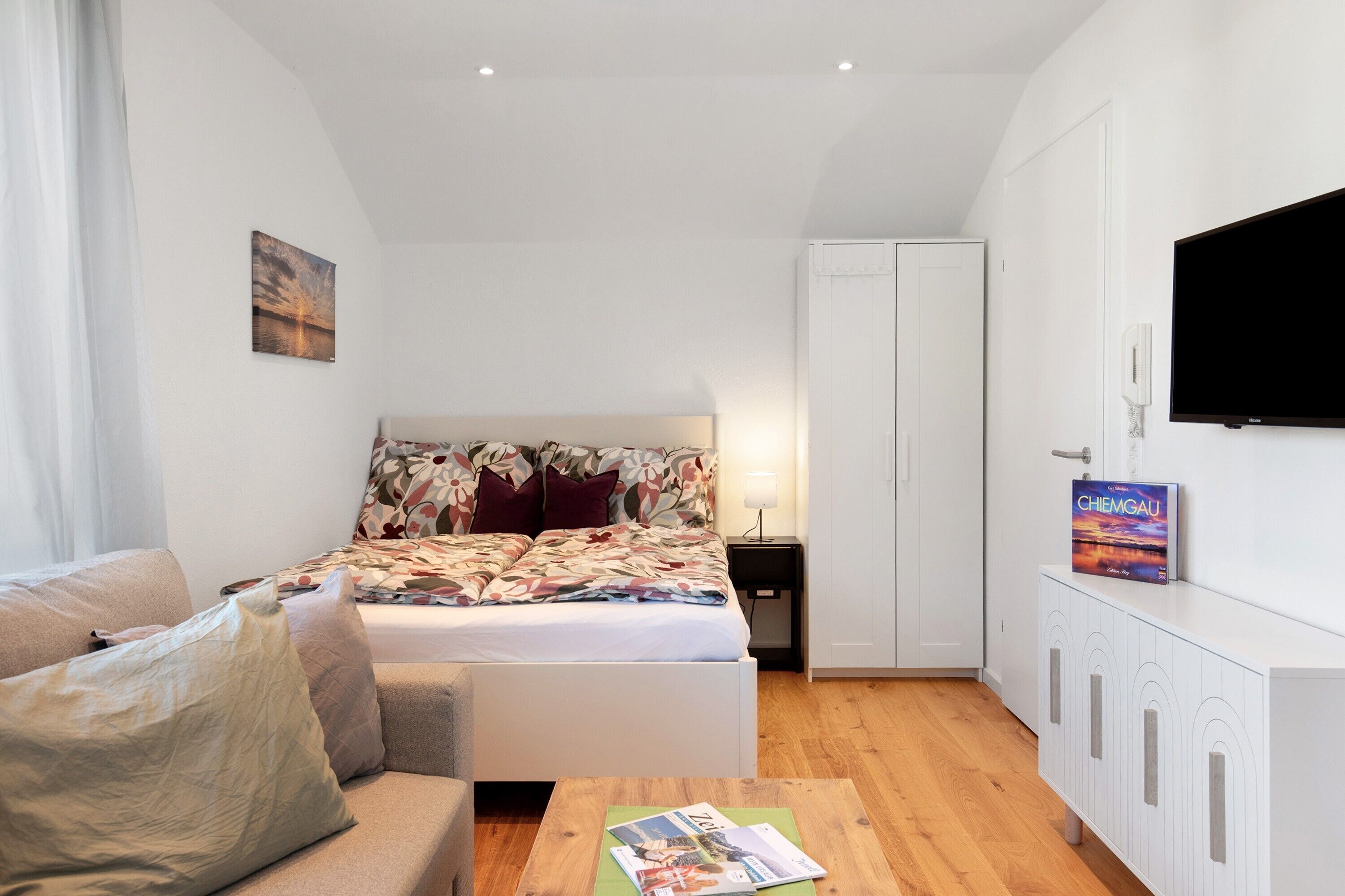 Un dormitorio con cama, mesita de noche, televisor, armario y una revista sobre la mesa.
