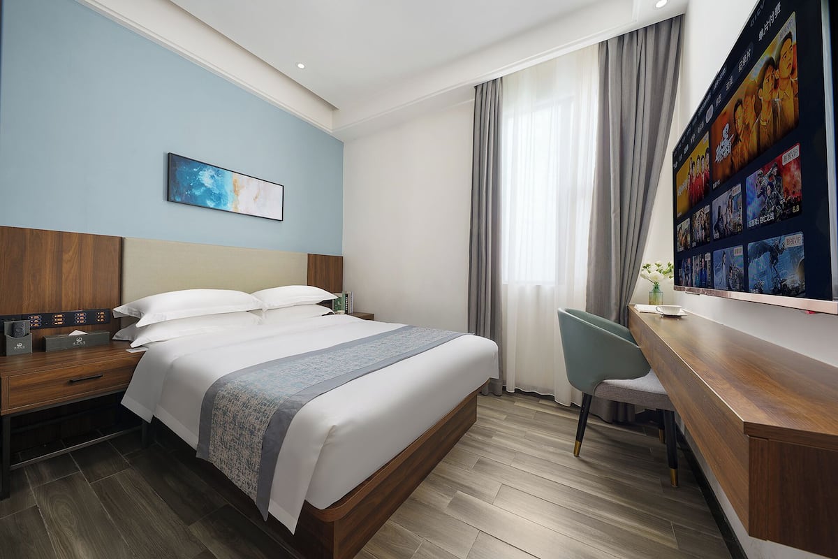A hotel room with a bed, bedside table, desk, chair, and a wall with movie posters.