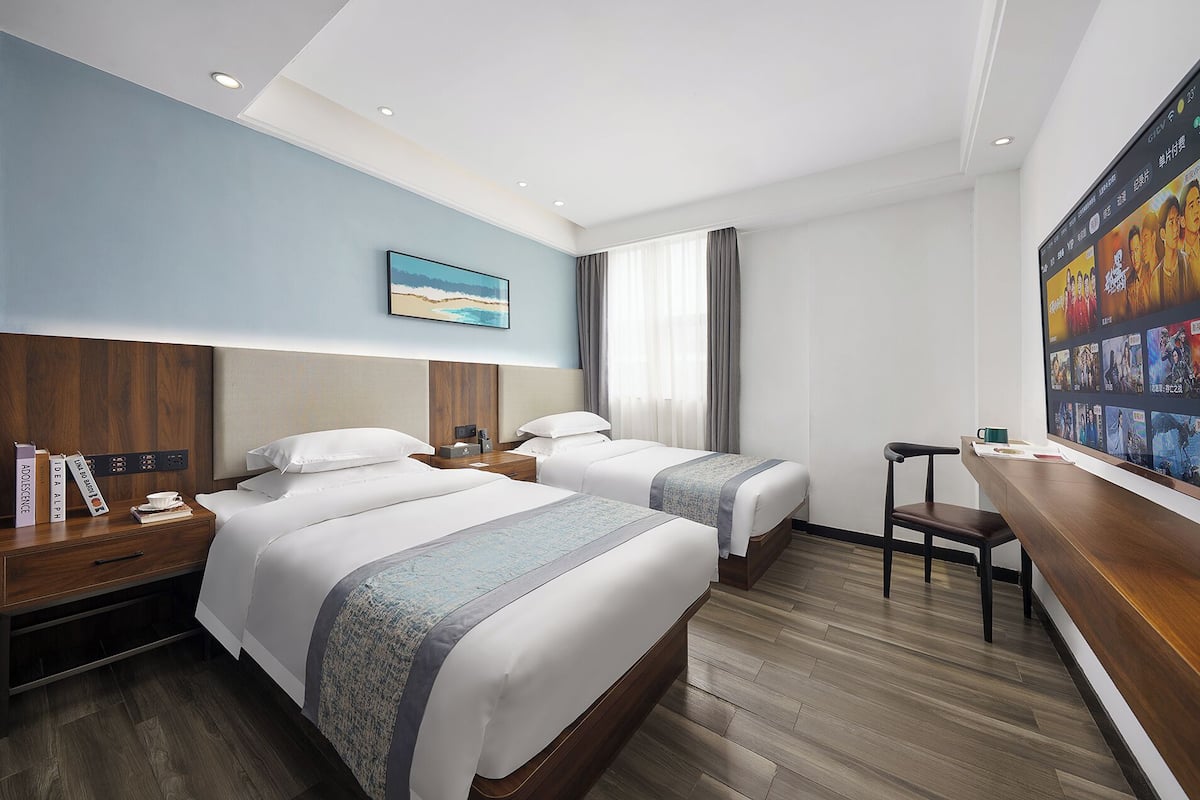 A hotel room with two beds, a desk, a chair, a TV, and a painting on the wall.