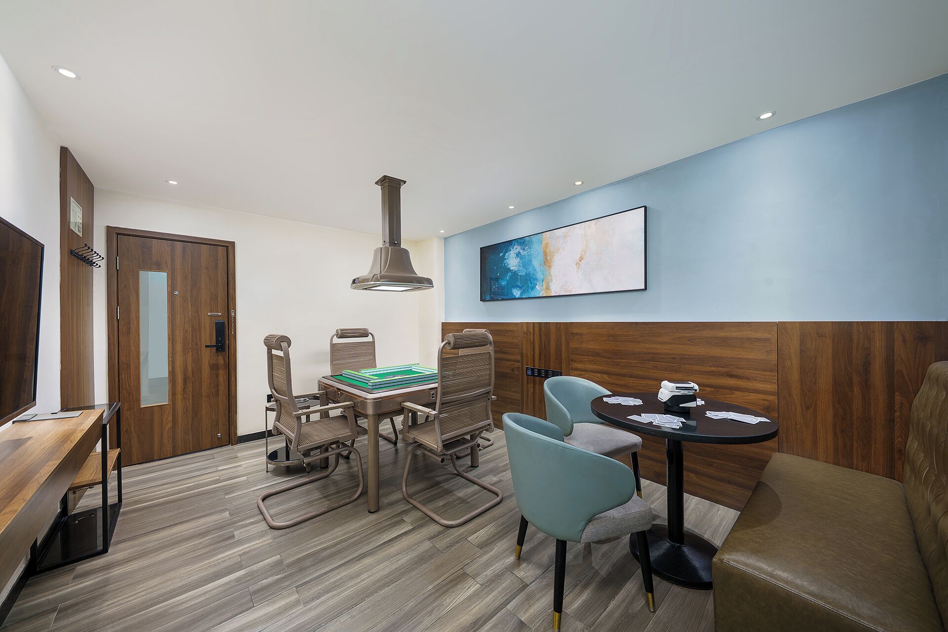 A modern hotel room with a wooden floor, a dining area with a table and chairs, a large window, and a painting on the wall.