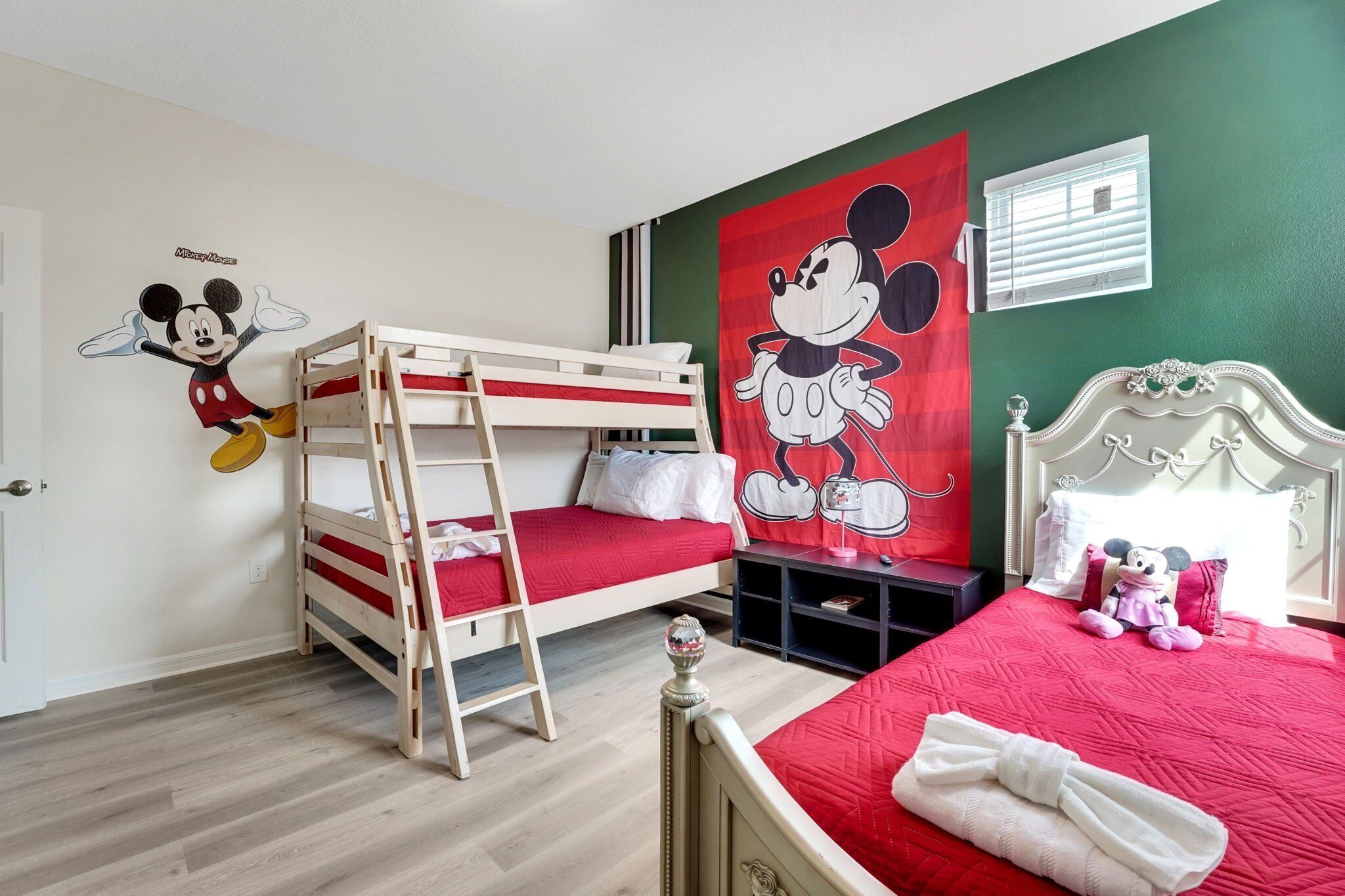 Habitación infantil con literas, un adhesivo de pared de Mickey Mouse y un peluche de Minnie Mouse.