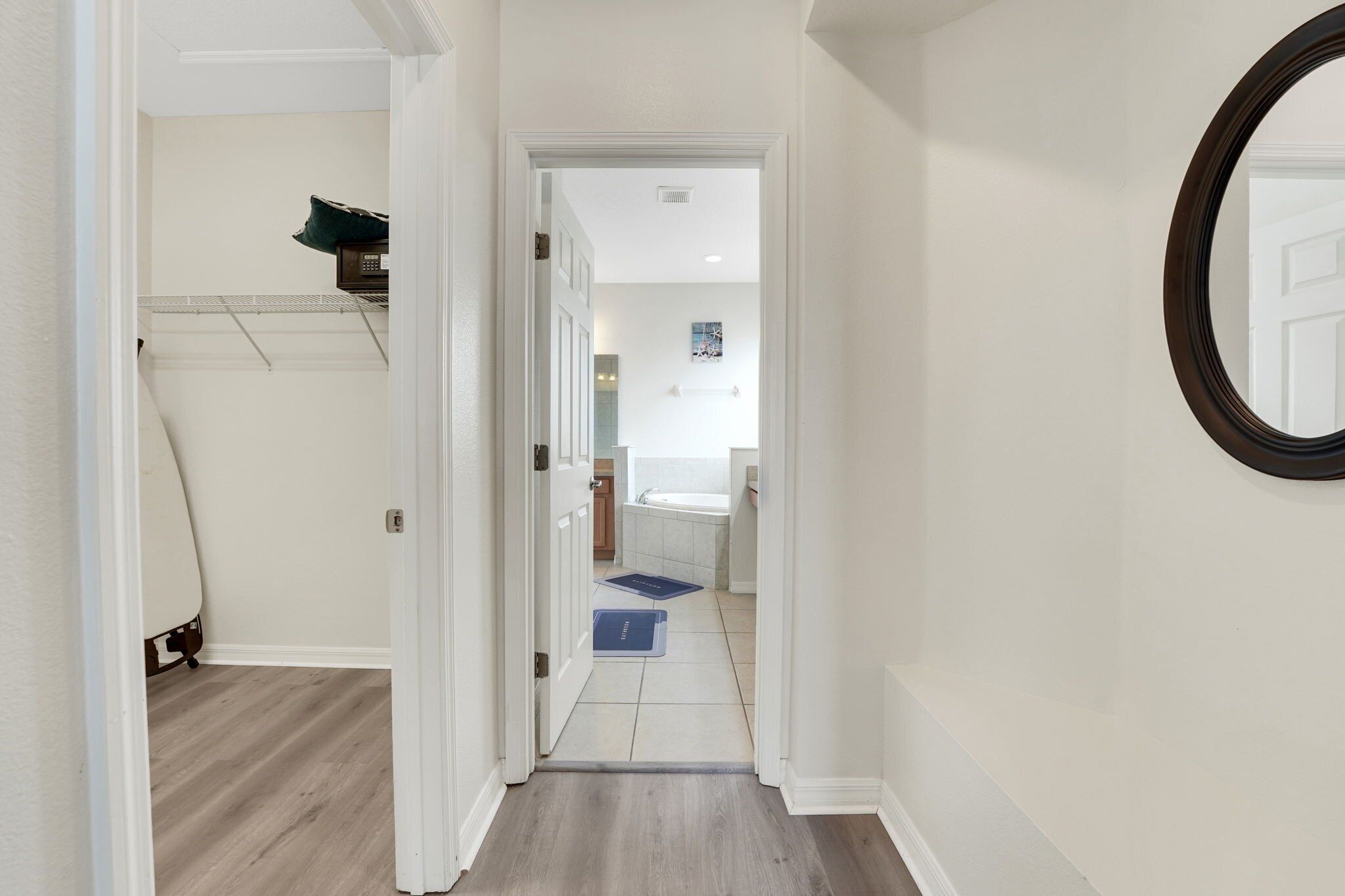 A hallway leading to a bathroom with a white door, a mirror on the wall, and a blue mat on the floor.
