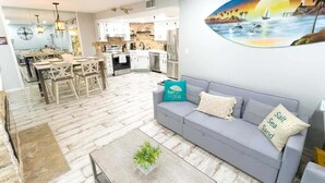 Ein modernes Wohnzimmer mit grauem Sofa, einem Couchtisch mit Pflanze und einem Essbereich mit Holzkombinationen.